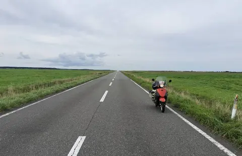 北海道のエヌサカ線と原付。地平線まで道路が延びているような様子と、道路わきの草原。
