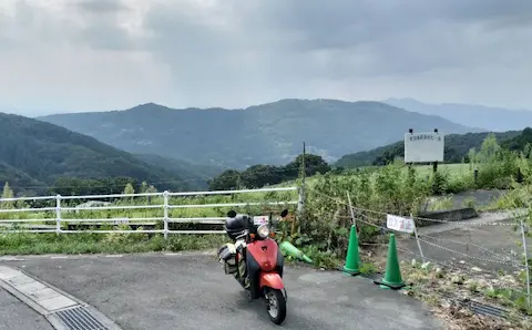 秩父山高原牧場の天空のポピー付近。山々の景色を背景に原付が停まっている。