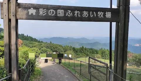 秩父山高原牧場のふれあい牧場入口。山々の景色とヤギが草原にいる。