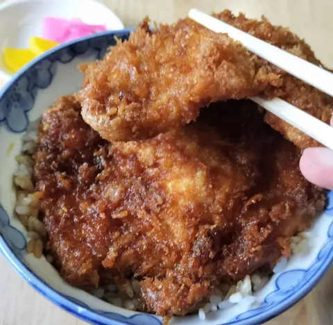 安田屋本店のわらじかつ丼。ソースがしみ込んだカツを箸で掴んでいる。