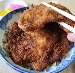 安田屋本店のわらじかつ丼。ソースがしみ込んだカツを箸で掴んでいる。