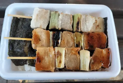 ハセガワストアの焼き鳥弁当。豚肉とネギが串にささって、ご飯の上に3本のっている。