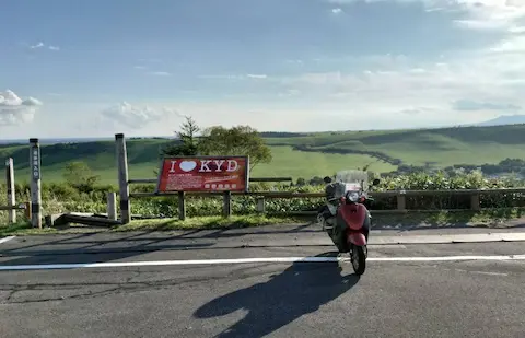 北海道の開陽台の駐車場風景。原付と草原や山々の景色が広がる。