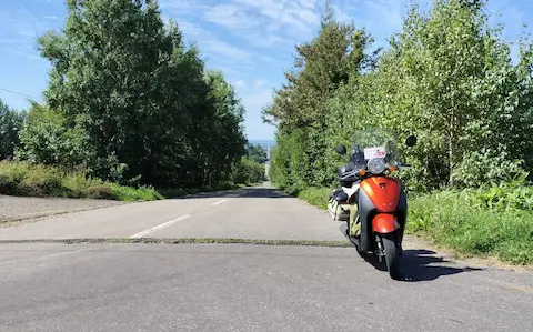 北海道の天に続く道。原付と木々に囲まれた真っすぐの続く道路。