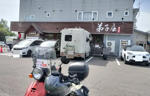 弟子屈ラーメン弟子屈総本店の外観写真。駐車場に原付と車が停まっている。