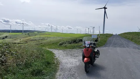 宗谷丘陵の景色。丘陵地の緑地の中に、風車が並ぶ。原付と写っている。