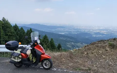 皇鈴山展望台の広場下。山々の景色を背景に原付が停まっている。